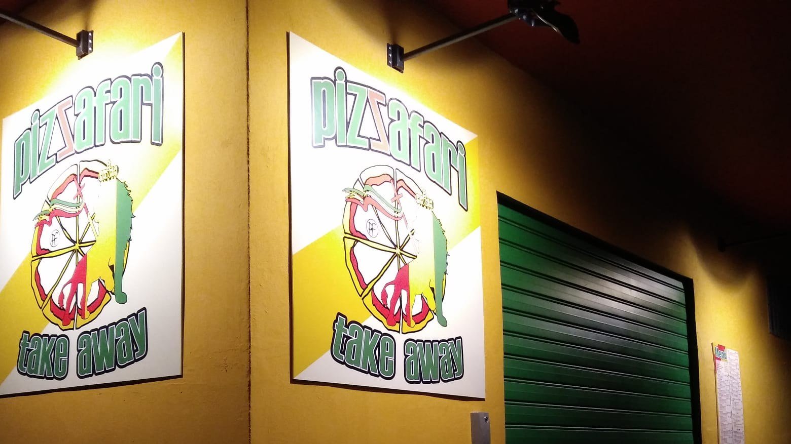 Letrero luminoso de Pizzafari take away en la fachada amarilla de la pizzería